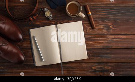 Arranging men's formal accessories: leather shoes, belt, watch, tie, pen, notebook and coffee, on dark rustic wood for a stylish Father's Day gift fla Stock Photo