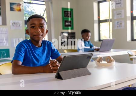African American schoolboys sitting in class, boy wearing blue tee using tablet, other using laptop Stock Photo
