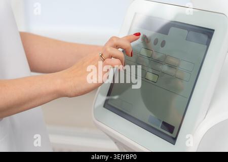 Close-up of a woman hand using a touchscreen on modern cosmetic equipment in a beauty clinic. Aesthetic treatment technology and skincare procedure co Stock Photo