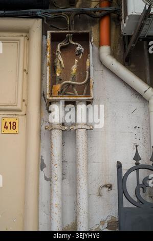 A weathered, neglected electrical junction box with exposed wires sits on a wall by unit 418, serving as a stark example of urban decay and the potent Stock Photo