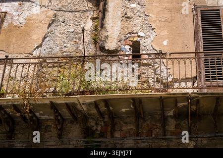 Nature has reclaimed this historic, decaying balcony. Wild weeds grow between the rusted iron railings, highlighting the passage of time and neglect u Stock Photo