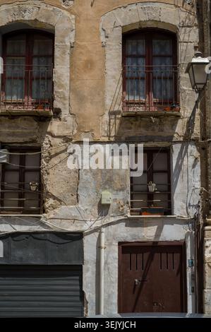 This weathered building facade captures the passage of time on a historic city street, featuring aged plaster, shuttered windows, and iron balconies i Stock Photo