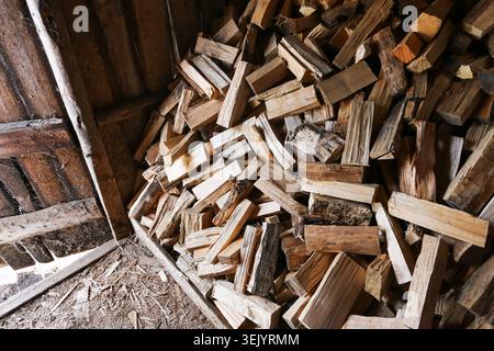 Large stack of chopped firewood stored in barn. Wooden logs prepared for winter heating and fuel supply concept. Stock Photo