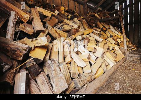 Firewood stacked inside wooden shed closeup. Prepared chopped logs for home heating and winter fuel storage concept. Stock Photo