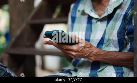 Elderly person's hands holding smartphone, interacting with digital technology Stock Photo