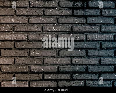 Horizontal view of a modern dark charcoal brick wall. The bricks have a rough, weathered texture with small white flecks, creating a rustic yet contem Stock Photo