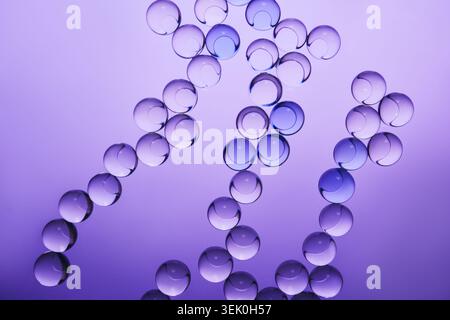 Clear and blue spheres forming an abstract chains on gradient purple surface Stock Photo