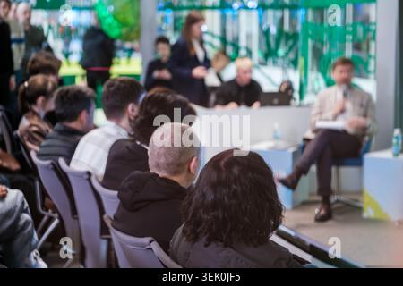 Audience listens to panel discussion at modern conference, speaker presents while attendees follow and take notes. Stock Photo