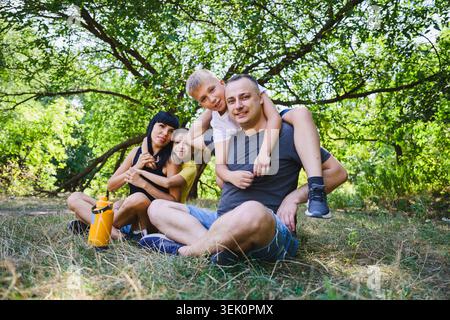 Parents and two sons enjoying a sunny day in the park. Happy family relaxing outdoors, sharing playful moments and quality time surrounded by nature. Stock Photo