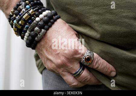 A  close-up of a person's hand adorned with multiple bracelets and rings. The bracelets, made of black lava beads, stones, and metallic elements, are Stock Photo