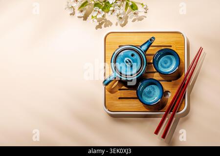 Blue ceramic teapot with blooming spring branch on wooden tray in minimal asian style composition Stock Photo