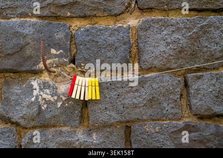 Vibrant red, white, and yellow clothespins hang on a wire against a stone wall, ready to hold laundry for drying. It is a simple tool used for everyda Stock Photo