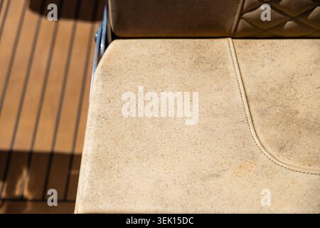 The textured surface of a worn boat seat shows signs of age and use, contrasting with the smooth wooden planks of the deck Stock Photo