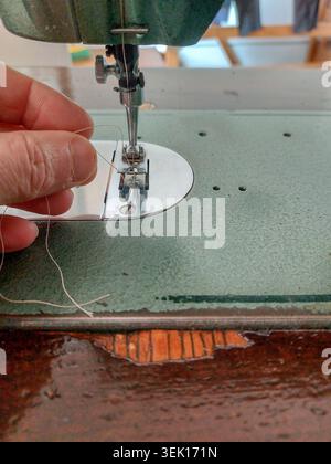 Detail shot of a man's hand preparing a classic sewing machine mechanism, focusing on the precision and concentration involved in home crafting, tailo Stock Photo