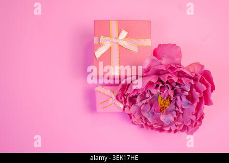 A soft and elegant flat lay featuring a vibrant pink peony paired with pastel gift boxes, set against a harmonious pink background Stock Photo
