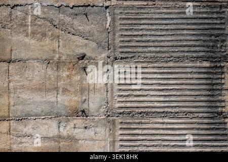 Close-up of a concrete wall displaying contrasting textures. Left side features rough surface with rusty nails and a diagonal crack, while the right s Stock Photo