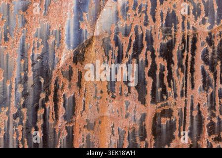 Abstract close-up view of weathered corrugated metal surface with extensive rust. Dark oxidized areas contrast with reddish-brown rust patches, showca Stock Photo