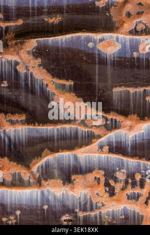 Close-up of a corrugated metal surface showcasing extensive rust and oxidation. Textured with vertical ridges, orange and brown patches create an abst Stock Photo
