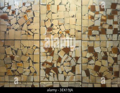 Close-up view of a mosaic surface made from broken ceramic tiles. Irregular fragments in cream, beige, and brown tones create a weathered texture, ide Stock Photo