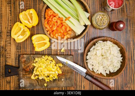 Vegetables are prepared on a wooden table. Yellow pepper slices are next to chopped onions and diced yellow bell peppers. Celery sticks and carrot pie Stock Photo