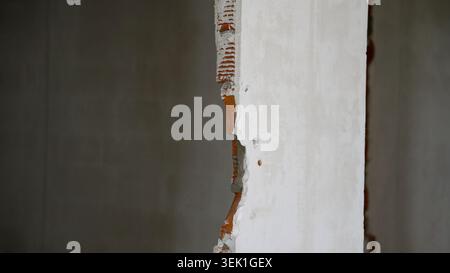 Damaged white plaster wall with exposed red brick edge and small hole Stock Photo