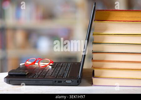 Laptop computer and stack of books ,blurred office in the background.Beat the clock,office work,research,education concept.Free copy space. Stock Photo