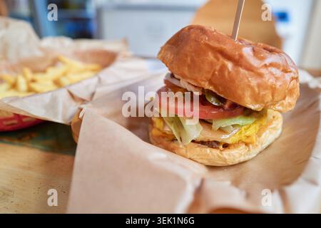A close up of a handmade hamburger on parchment paper. A glossy bun, juicy patty, cheese, and fresh tomato highlight this appetizing gourmet meal. Stock Photo