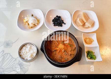 Korean Cheonggukjang, fermented soybean stew, in an earthenware pot served with white rice and side dishes. Authentic and rustic everyday dining. Stock Photo
