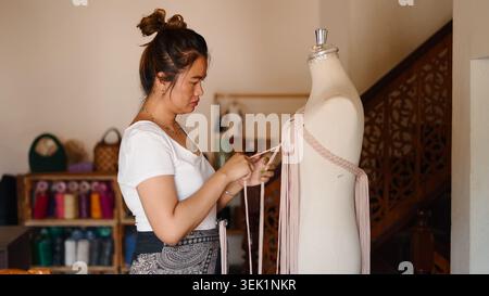 Woman tying macrame garment on mannequin, creating handmade fashion Stock Photo