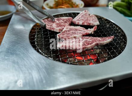 Raw, marbled beef sirloin prepared for Korean BBQ. The meat is served on a metal plate and placed over glowing charcoal, showing an authentic vibe. Stock Photo