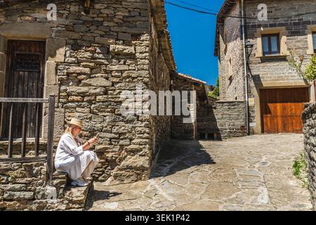 Woman using smartphone while resting in medieval stone village of Rupit, Catalonia, Spain, sitting on historic street Stock Photo