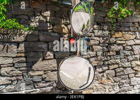 Traffic light and convex mirrors mounted on stone wall in medieval mountain village Stock Photo
