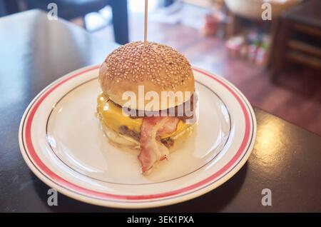 A close-up of a gourmet beef burger featuring melted cheese, bacon, and caramelized onions on a sesame bun, served on a classic white plate. Stock Photo