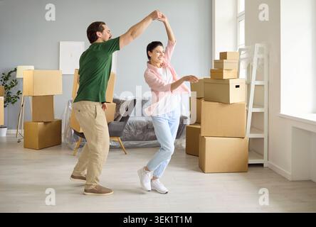 Happy couple dancing among moving boxes in bright new apartment, celebrating home Stock Photo