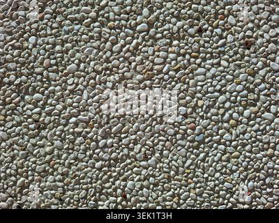 A surface shows a top down view of exposed aggregate concrete made with closely packed gray and white pebbles. This surface may be seen in sidewalks o Stock Photo