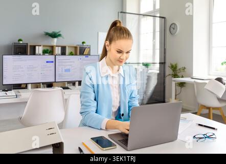 Young financial analyst businesswoman typing on laptop at modern office desk Stock Photo