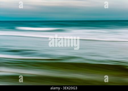 Long exposure captures rolling ocean waves as soft turquoise and green streaks beneath a muted sky. Stock Photo