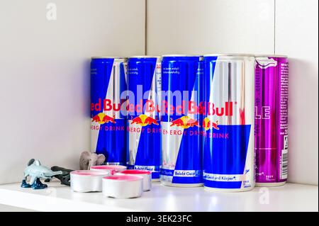 Augsburg, Germany — May 31 2026: Several Red Bull energy drink aluminum cans arranged on a white shelf next to small animal figures and pink tealight Stock Photo