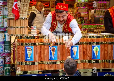 A male vendor in traditional red and white Ottoman costume stands proudly at his colorful spice and goods stall inside the Grand Bazaar, Istanbul, Tur Stock Photo