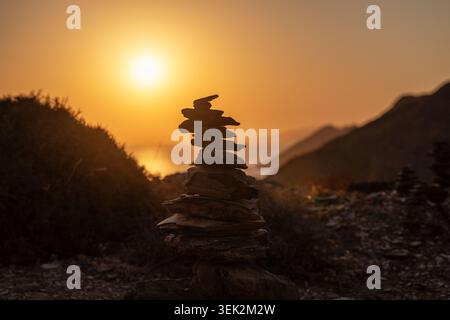 Balanced stack of zen stones at golden hour with colorful sky and sea in background, Crete island, Greece. Peaceful coastal scene symbolizing harmony, Stock Photo