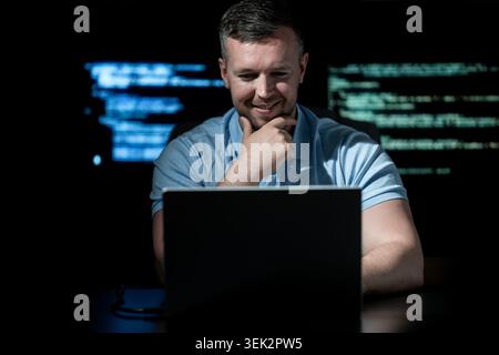 Programmer writes code on laptop. Programmer analyzes system security data. Programmer monitors network activity. Programmer detects cyber attack Stock Photo