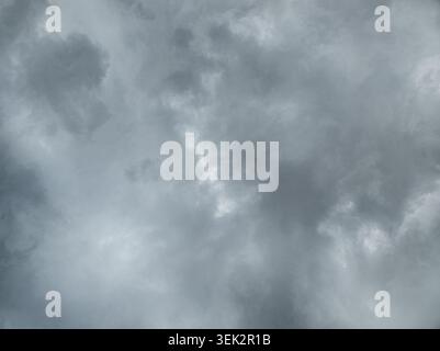 Low-angle view of a sky filled with dense, textured clouds. Sunlight filters through some areas, creating highlights against darker formations, suggesting impending weather change. Stock Photo