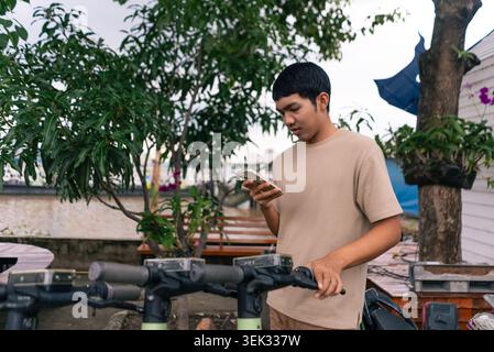Young man renting electric scooter using smartphone app for urban transport Stock Photo