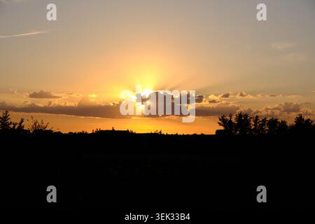 Beautiful dramatic sunset sky with golden sun rays breaking through dark clouds over silhouette Stock Photo
