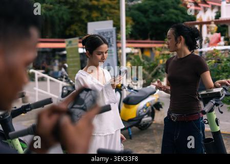 Young women using smartphones, interacting at city scooter sharing station Stock Photo
