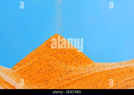 Abstract minimalist composition showing orange sand forming pyramid dune against blue sky Stock Photo