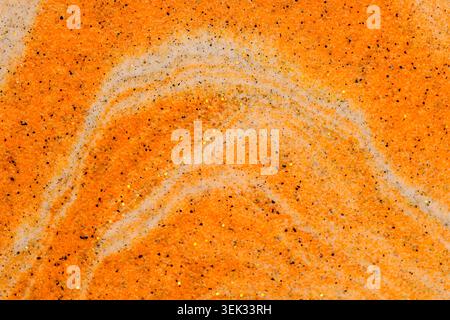 Close up textured abstract background with golden orange sand swirls and black sparkly glitter Stock Photo