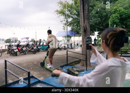 Woman filming man riding electric scooter for content creation and urban lifestyle Stock Photo