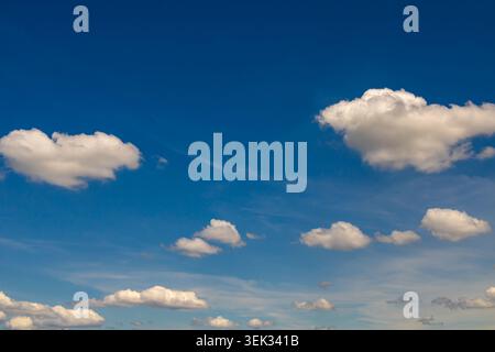 Expansive blue sky filled with soft scattered cumulus clouds during a bright sunny day with calm atmospheric scenery. Stock Photo