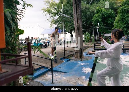 Young couple enjoying outdoor activity, woman filming man riding electric scooter Stock Photo
